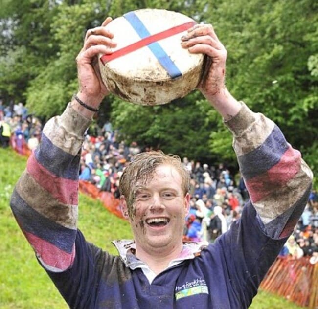 jóven ganador del campeonato cheese rolling sosteniendo el queso rodante